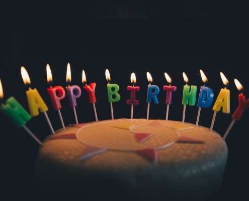 Foto: kleiner Torte mit brennenden Kerzenbuchstaben die die Worte Happy Birthday bilden