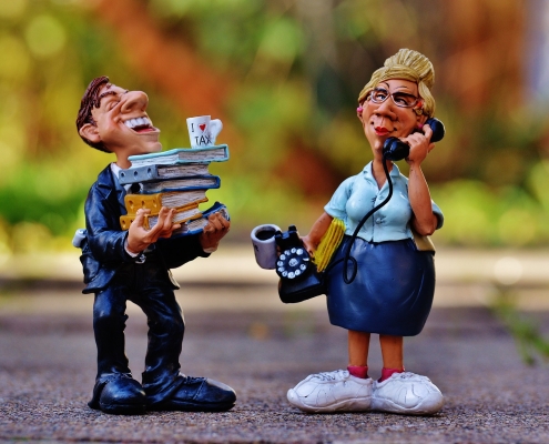 Foto: 2 Plastik-Figuren - lachender Mann mit Heftern auf beiden Unterarmen und telefonierende Frau mit altem Telefon